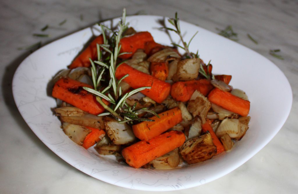 Plate of caramelized oven-roasted vegetables with a piece of rosemary