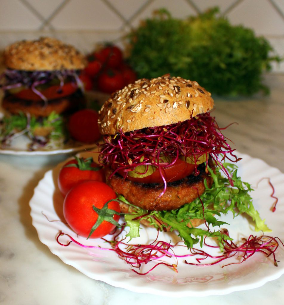 Eggplant and sundried tomato vegan burger in a bun with vegetables and pink sprouts