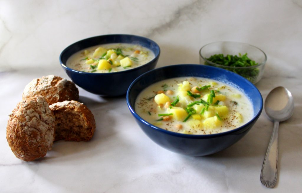 Two bowls of soup, bread and chives next to them